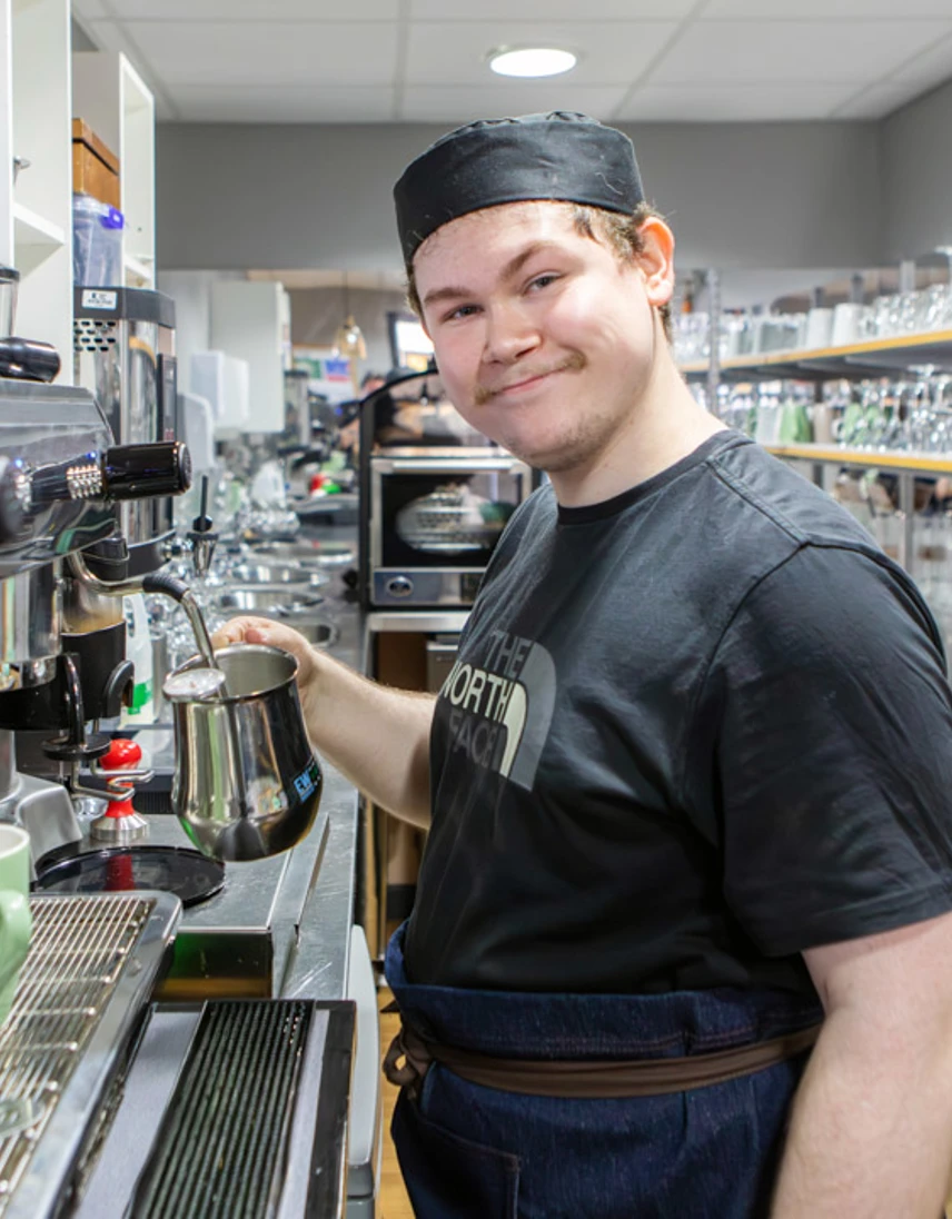 Barista student smiling while preparing a coffee beverage at an espresso machine. Barista student smiling while preparing a coffee beverage at an espresso machine.